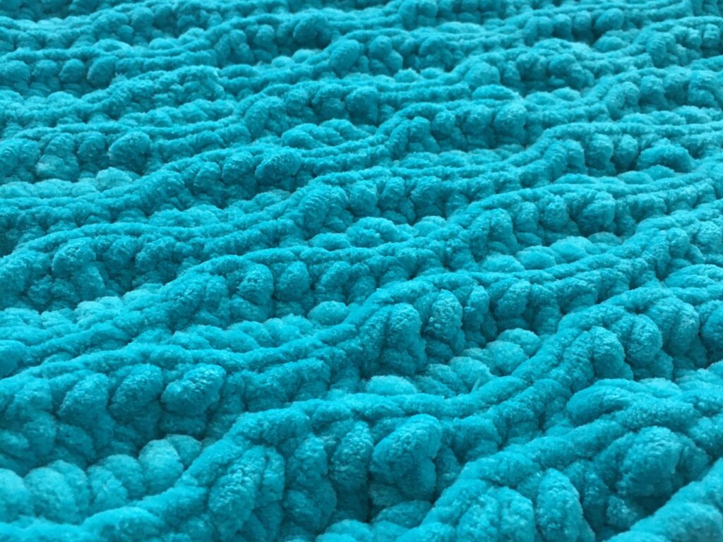 Crochet Flat lay of a blue plush chunky crochet blanket made out of chenille yarn using the almond ridges stitch pattern of slip stitch and half double crochet close up