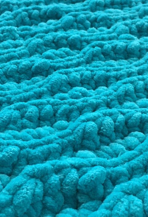 Crochet Flat lay of a blue plush chunky crochet blanket made out of chenille yarn using the almond ridges stitch pattern of slip stitch and half double crochet close up