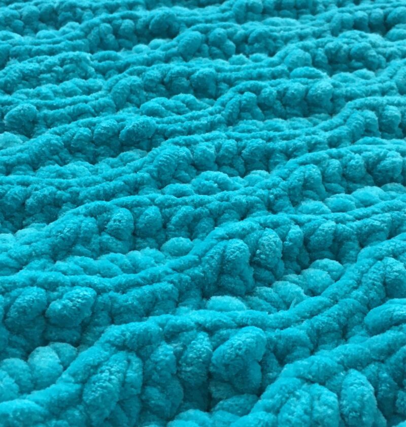 Crochet Flat lay of a blue plush chunky crochet blanket made out of chenille yarn using the almond ridges stitch pattern of slip stitch and half double crochet close up