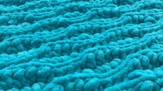 Crochet Flat lay of a blue plush chunky crochet blanket made out of chenille yarn using the almond ridges stitch pattern of slip stitch and half double crochet close up