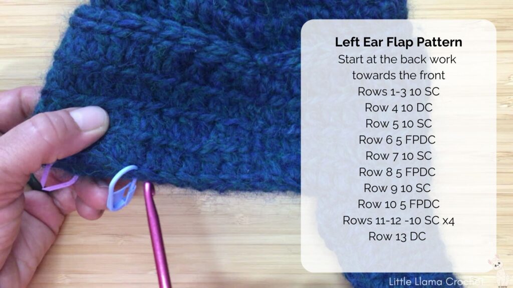 A screen grab of the video tutorial with the blue crochet baby hat in progress. One right ear flap is completed and the hands and hook are pointing to the space where the left ear flap will go. Written instructions for the ear flap appear on the right hand side of the screen.